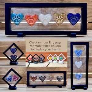 May include: A display case with five heart-shaped ornaments in shades of blue, red, white, and brown, each featuring a paw print design. The case is dark blue and has a clear front. The text reads: "Check out our Etsy page for more frame options to display your hearts."