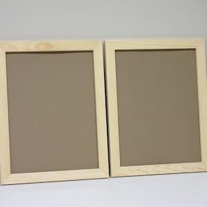 May include: Two natural wood picture frames with brown cardboard backing. The frames are side by side on a white surface.