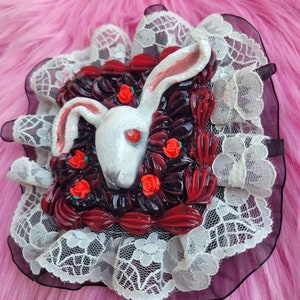 以下が含まれることがあります： 赤い目をした白いウサギが、赤いバラと黒い葉に囲まれています。ウサギは、白いレースの縁取りが施された正方形のフレームの中にいます。