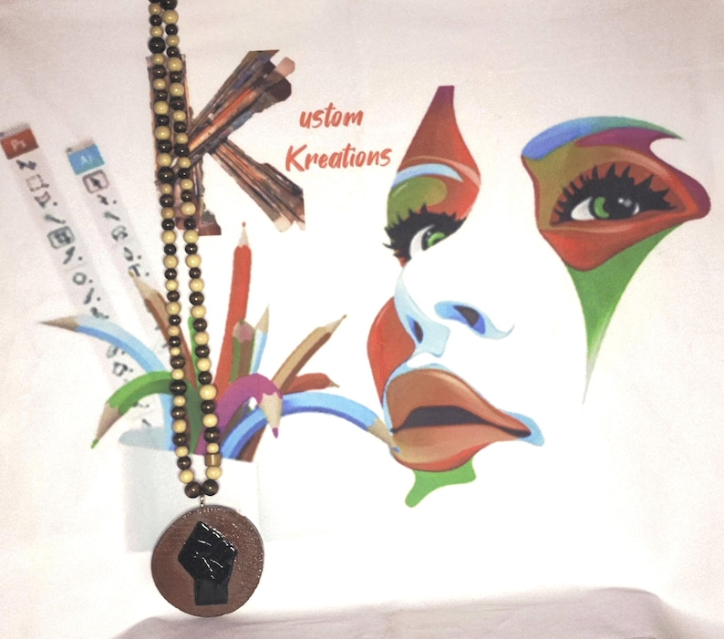 May include: A wooden beaded necklace with a round pendant featuring a black fist. The background includes a colorful artistic face and the text "ustom Kreations". Pencils and art supplies are also visible.