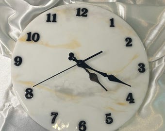 May include: A white and gold marble clock with black hands and black numbers. The clock face has a white background with gold swirls.