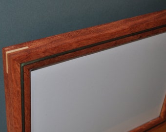 Op de afbeelding: Een houten fotolijst met een donkerrode mahonie afwerking en een dunne groene inleg. De lijst heeft een witte passe-partout en een helder glazen voorpaneel.