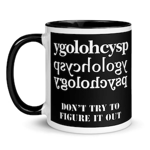 May include: A white ceramic mug with a black interior and handle. The mug features the word "psychology" spelled backward in white text, along with the phrase "DON'T TRY TO FIGURE IT OUT" in white text on a black background.