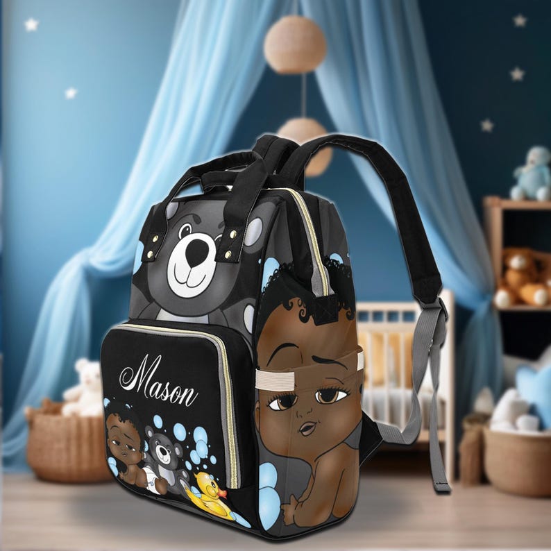 May include: Black and gray diaper bag with a bear and baby graphic. The bag features a front pocket with the name "Mason" and illustrations of babies and a rubber duck. It has a top handle and adjustable shoulder straps.