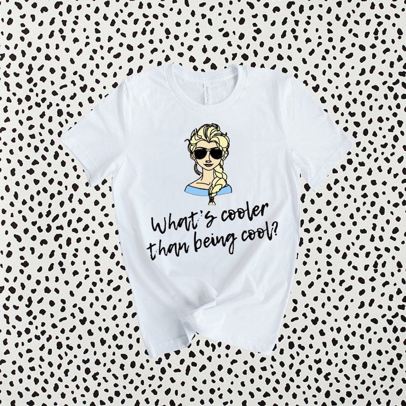 May include: White t-shirt with a cartoon image of a woman with blonde hair wearing sunglasses and a blue dress. The text "What's cooler than being cool?" is printed below the image.
