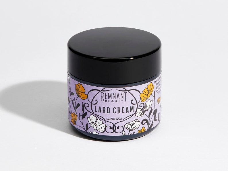 May include: A white jar with a black lid and a floral design. The jar is labeled "Remnant Beauty Lard Cream" and "Net Wt. 60 ml".
