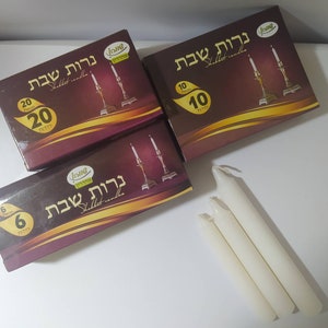 Peut inclure: Trois boîtes de bougies de Shabbat avec des quantités variables, ainsi que plusieurs bougies blanches. Les boîtes sont marron avec des accents dorés et du texte hébreu. Les boîtes contiennent 6, 10 et 20 bougies.