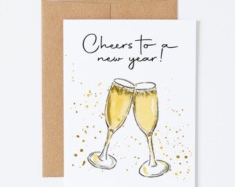 May include: Greeting card with a watercolor illustration of two champagne flutes clinking, with gold accents and the text "Cheers to a new year!". Includes a brown envelope. Perfect for New Year's celebrations.