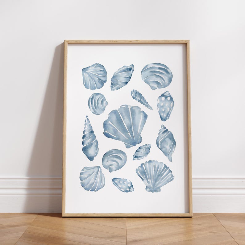 Puede incluir: Una impresi&oacute;n enmarcada con una colecci&oacute;n de conchas marinas azules en acuarela. La obra de arte muestra varias formas y tama&ntilde;os de conchas, creando un tema costero. Las conchas est&aacute;n pintadas en tonos azules sobre un fondo blanco, enmarcadas en madera clara.
