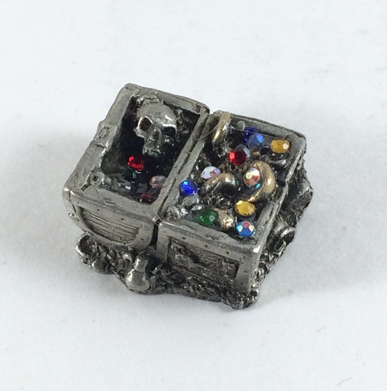 May include: A pewter treasure chest with a skull on the lid, filled with colorful gems and gold coins. The chest is open and the gems are visible.