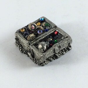 May include: A small pewter treasure chest with a skull on the lid, open to reveal a variety of colorful gems and jewels.
