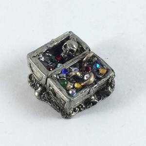 May include: A pewter treasure chest with a skull on the lid, open to reveal a variety of colorful gems and gold coins.
