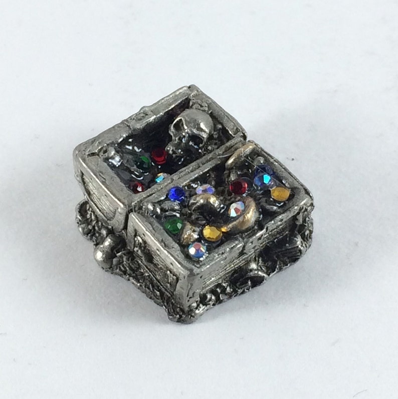 May include: A pewter treasure chest with a skull on the lid, open to reveal a variety of colorful gems and gold coins.