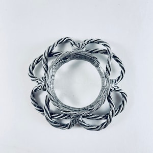 May include: A silver ring with a rope-like design. The ring is circular and has a raised center.