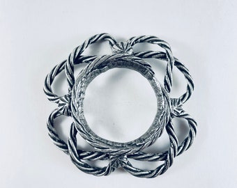 May include: A silver ring with a rope-like design. The ring is circular and has a raised center.