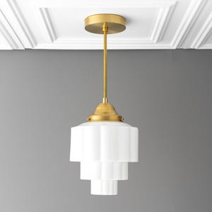 May include: A white glass pendant light with a gold finish and a geometric design. The light is hanging from a ceiling with white molding.