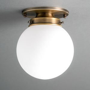 May include: A brass ceiling light fixture with a white frosted glass globe.