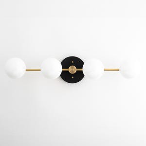 May include: A modern wall sconce with four white globe light bulbs and a black circular base. The sconce has a gold metal bar connecting the bulbs.