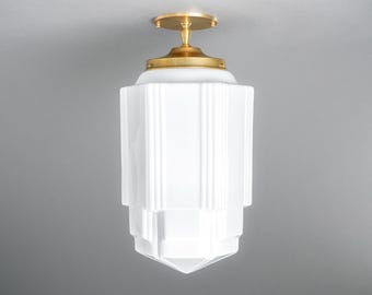 May include: A white glass ceiling light fixture with a brass finish. The light has a geometric design with a square base and a pointed top.