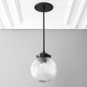 May include: Black pendant light with a clear ribbed glass globe shade.