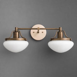 May include: A two-light wall sconce featuring a horizontal antique brass metal bar and a circular wall mounting plate. Two white glass bowl-shaped shades are suspended from the bar by curved metal arms, creating a symmetrical lighting fixture.