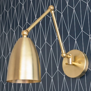 May include: A gold-toned wall-mounted light fixture with a swivel arm and a round, bell-shaped shade.
