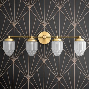 May include: A gold four-light bathroom vanity light fixture with clear glass shades. The shades have a textured, ribbed design.