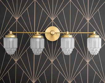 May include: A gold four-light bathroom vanity light fixture with clear glass shades. The shades have a textured, ribbed design.