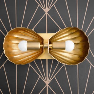 May include: A pair of gold-toned wall sconces shaped like seashells with white light bulbs. The sconces are mounted on a black geometric patterned wall.