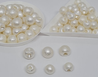 May include: A collection of white pearl-like buttons in two bowls. The buttons are round and have a textured surface. There are also seven buttons laid out on a white surface.