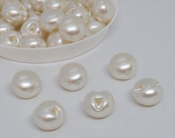 May include: A bowl of white pearl buttons, with a few buttons scattered on a white surface.
