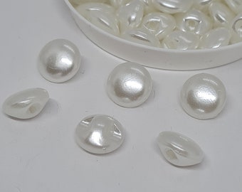 May include: A close-up of six white pearl-like buttons with two holes each. The buttons are arranged on a white surface.