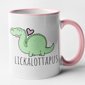 May include: White ceramic mug with a pink rim and handle. The mug features a cartoon green dinosaur with a pink heart and the text "LICKALOTTAPUS".
