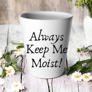 May include: White ceramic planter with black text that reads "Always Keep Me Moist!"