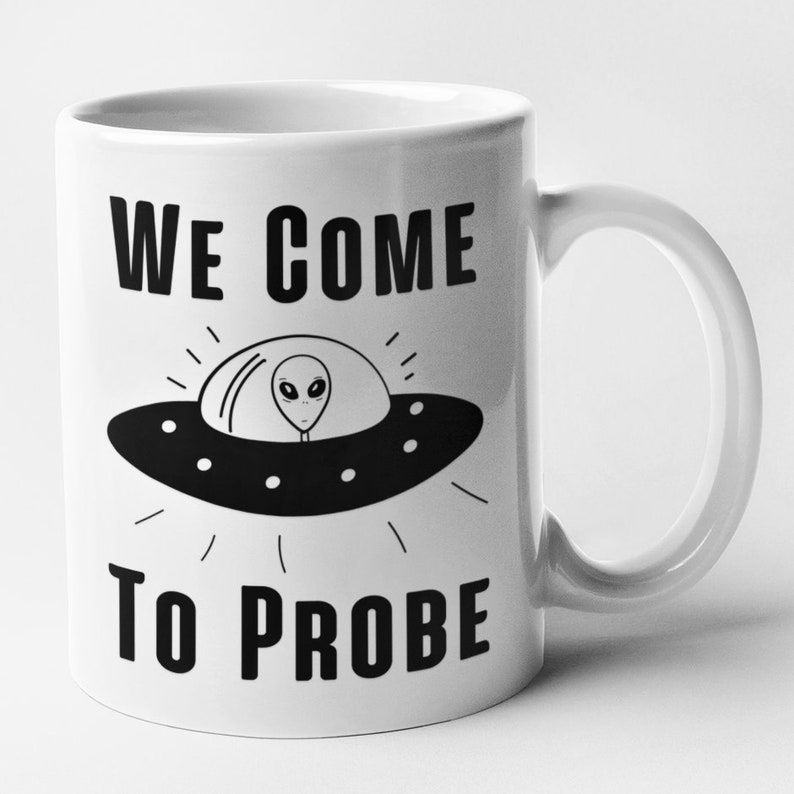 Op de afbeelding: Witte keramische mok met een zwart-witte illustratie van een UFO met een alien erin. De tekst "WE COME TO PROBE" staat op de mok gedrukt.