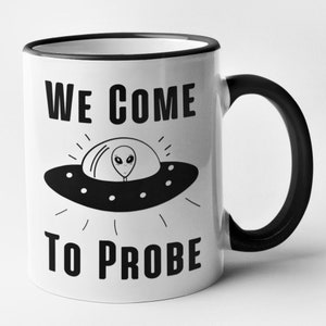 Op de afbeelding: Witte keramische mok met een zwarte rand en handvat. De mok heeft een zwart-witte illustratie van een UFO met een alien erin. De tekst "WE COME TO PROBE" staat op de mok gedrukt.