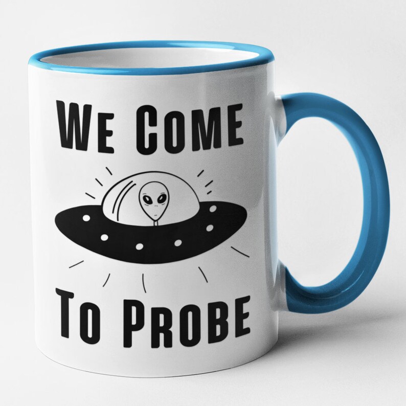 Op de afbeelding: Een witte keramische mok met een blauwe rand en handvat. De mok heeft een zwart-witte illustratie van een UFO met een alien erin. De tekst "WE COME TO PROBE" staat op de mok gedrukt.