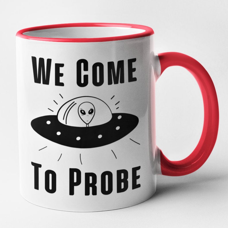 Op de afbeelding: Witte keramische mok met een rode rand en handvat. De mok heeft een zwart-witte illustratie van een UFO met een alien erin. De tekst "WE COME TO PROBE" staat op de mok gedrukt.