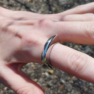 May include: A silver ring with a unique curved design. The ring is made of smooth metal and has a polished finish.