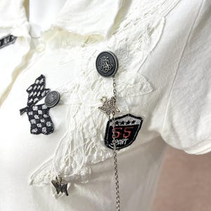 Polo bianca a maniche corte con inserti patchwork, ciondoli a farfalla in pizzo e dettagli di paillettes in stile grunge Y2K.
