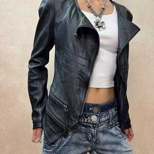 May include: A black leather jacket with an asymmetrical front zipper, long sleeves, and two diagonal zippered pockets on the lower right side. The jacket features horizontal stitched detailing on the front and is worn over a white tank top.