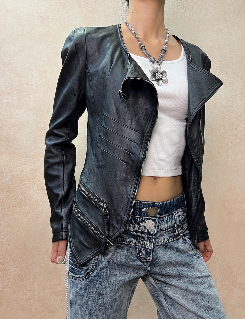 May include: A black leather jacket with an asymmetrical front zipper, long sleeves, and two diagonal zippered pockets on the lower right side. The jacket features horizontal stitched detailing on the front and is worn over a white tank top.
