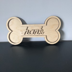 May include: A wooden dog bone shaped sign with the name "hank" written on it.
