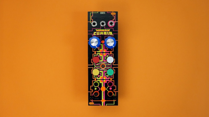 以下が含まれることがあります： 「YAKAM CUMBIA」というテキストとカラフルなデザインが施された黒いユーロラックモジュール。モジュールには4つのノブがあり、そのうち2つは青、1つは赤、1つは白、1つは黄、1つは緑です。