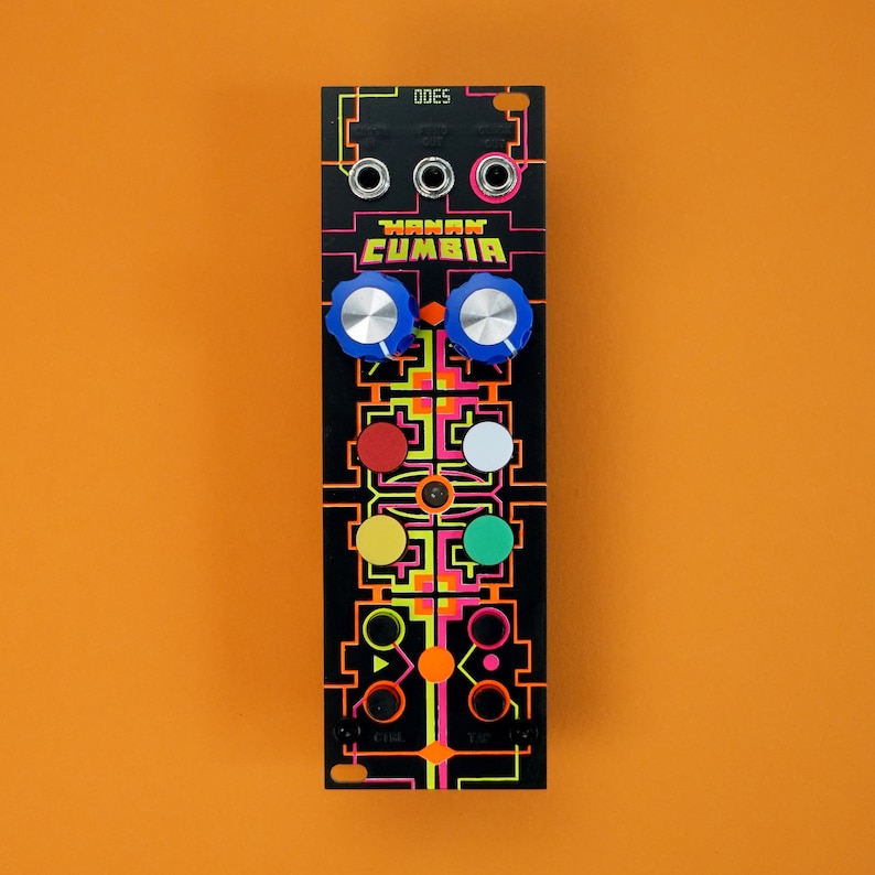 以下が含まれることがあります： 「OMAN CUMBIA」と「ODES」の文字が印刷された、黒と蛍光色のユーロラックモジュール。モジュールには、ノブ、ボタン、ジャックがいくつかあります。