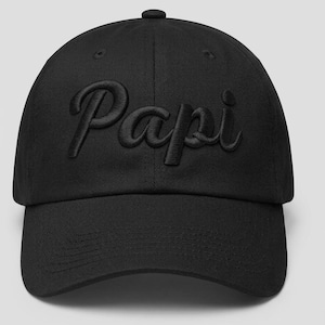May include: Black baseball cap with the word "Papi" embroidered in a cursive font. The cap has a curved brim and a button on top. The hat is made of a soft, durable material.