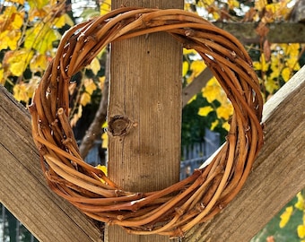 May include: A brown woven wreath made of twigs hangs on a wooden post. The wreath is round and has a rustic look.