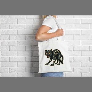 May include: White tote bag featuring a black cat illustration with exposed bones and glowing orange eyes. The cat is in a menacing pose, with its mouth open. The bag is held by a person.