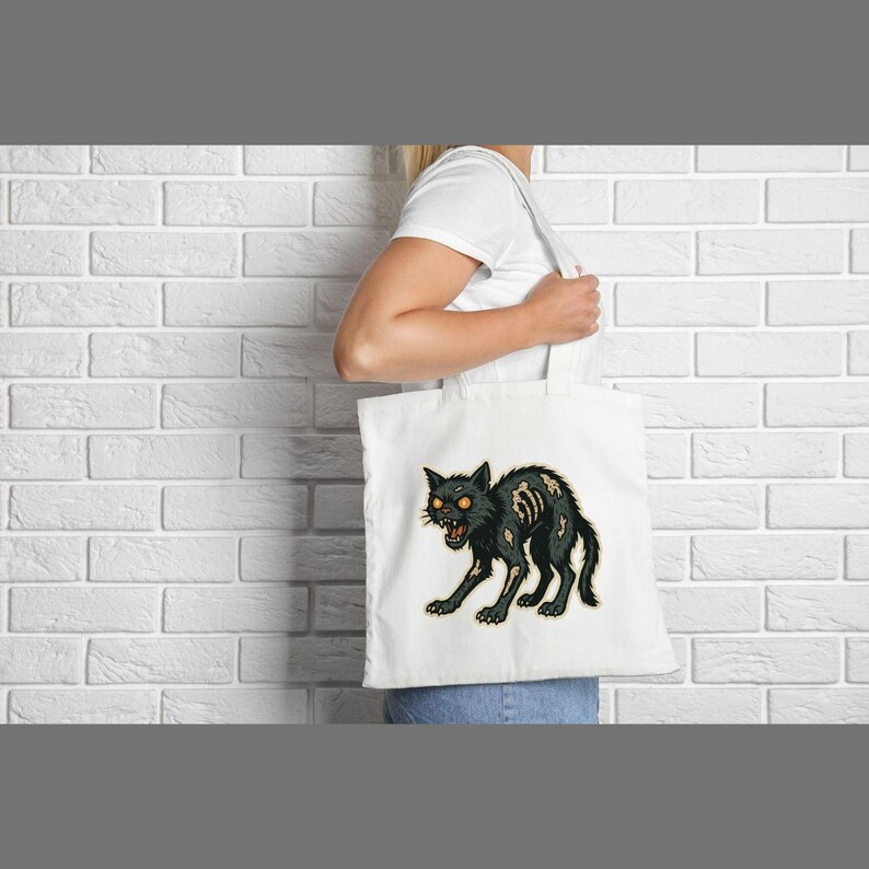 May include: White tote bag featuring a black cat illustration with exposed bones and glowing orange eyes. The cat is in a menacing pose, with its mouth open. The bag is held by a person.