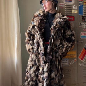 May include: A white ceramic mug with a black handle and the text "But First, Coffee" in a bold, black font. The mug is set against a blurred background, suggesting a cozy setting.